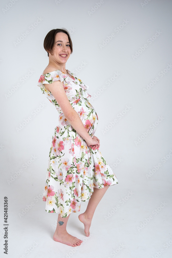 Studio portrait of cheerful young pregnant woman in summer dress on white gray background, happy pregnancy concept Studio portrait of cheerful young pregnant woman in summer dress on white gray background, happy pregnancy concept