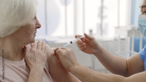 Crop view of male medical worker in protective mask disinfecting skin before giving vaccine shot in arm of retiree female person. Concept of vaccination, infectious disease prevention. photo