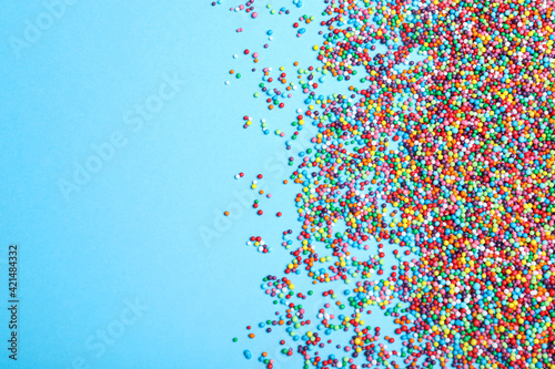 Colorful sprinkles on light blue background  flat lay with space for text. Confectionery decor