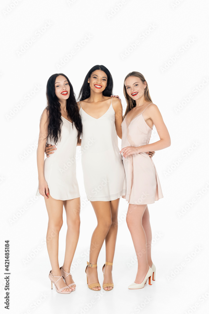 full length of cheerful interracial women with red lips standing in dresses isolated on white full length of cheerful interracial women with red lips standing in dresses isolated on white