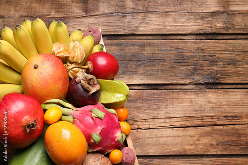 Crate with different exotic fruits on wooden table, top view. Space for text