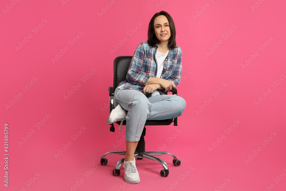 Mature woman sitting in comfortable office chair on pink background Mature woman sitting in comfortable office chair on pink background