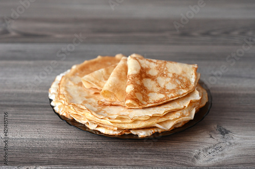 There is a plate of pancakes on the wooden table. Image with selective focus.