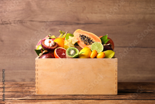 Different tropical fruits in box on wooden table