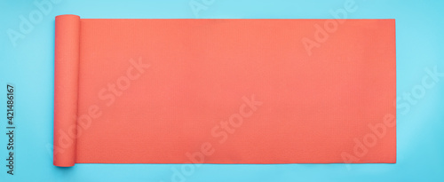 Minimal exercise and concept with pink fitness yoga mat on blue background. Horizontal banner size flat lay.
