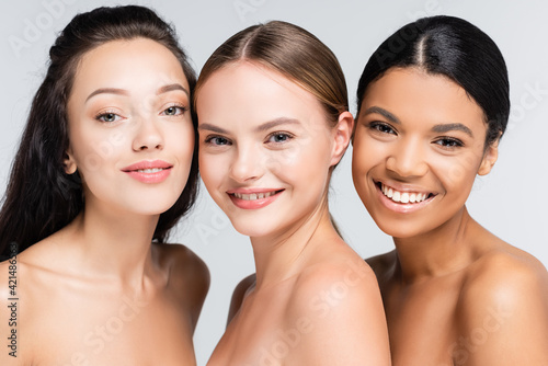 happy multiethnic women with bare shoulders isolated on grey