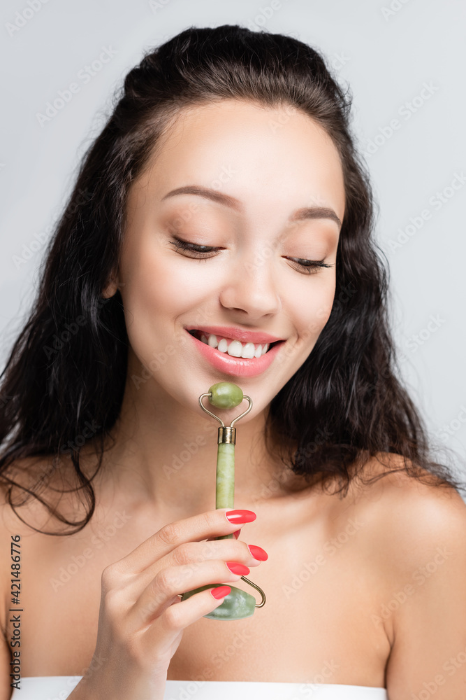happy woman using jade roller while massaging face isolated on grey happy woman using jade roller while massaging face isolated on grey