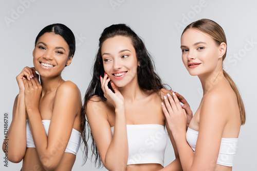 different and multiethnic women smiling isolated on grey