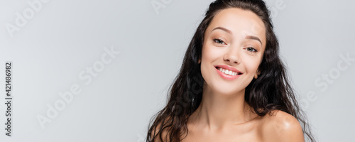 happy young woman with bare shoulders looking at camera isolated on grey, banner
