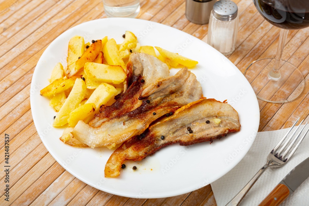 Appetizing roasted pork streaky bacon with side dish of baked potatoes..