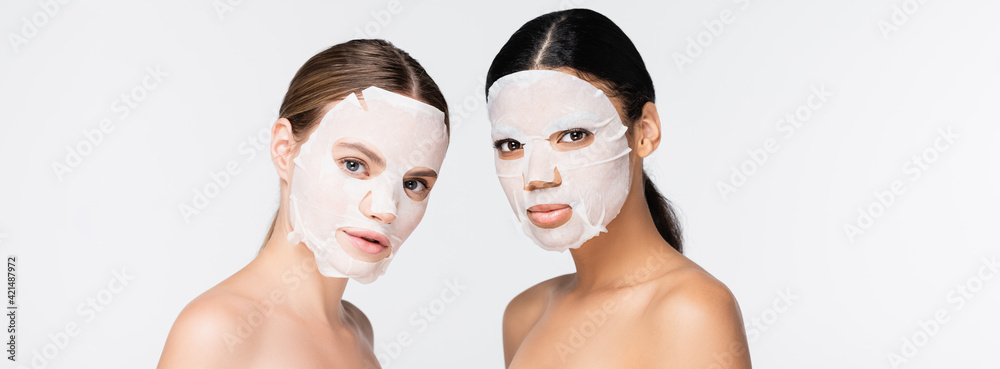 young interracial women in moisturizing sheet masks isolated on white, banner - obrazy, fototapety, plakaty 