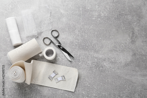 Fotografie Medical bandage rolls, sticking plaster and scissors on grey table, flat lay