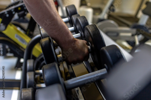 Closeup view of young man grabbing a dumbbell from a dumbbell rack in the fitness center. Muscular build sportsman taking weights from a rack in a gym. Shot of a man doing weight training at the gym.