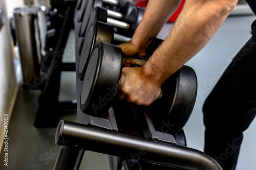 Cropped shot of a male athlete grabbing a set of dumbbells during his workout in the gym. Handsome and athletic young man working out with dumbbells in the gym. Man exercising with a dumbbell in a gym