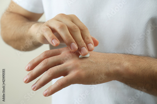 Man applying cream onto hand on beige background, closeup