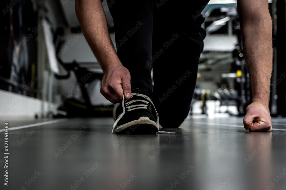 Fototapeta premium Unrecognizable man tying shoelace on sneakers, preparing for daily training. Shot of a unrecognizable man tying his shoelaces while exercising. Man crouching down and tying shoelaces before workout.