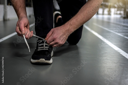 Unrecognizable man tying shoelace on sneakers, preparing for daily training. Shot of a unrecognizable man tying his shoelaces while exercising. Man crouching down and tying shoelaces before workout.