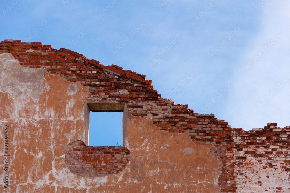 Red brick ruins of old building facade with window over blue sky background