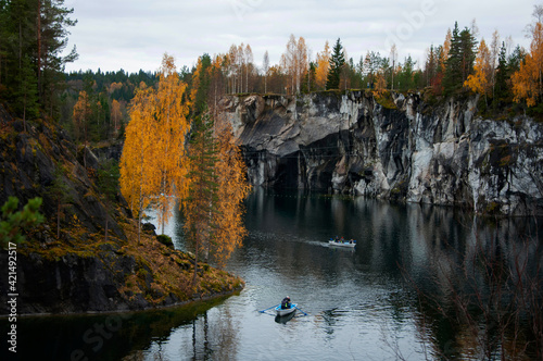 Tourist boats in dark pond at marble canyon with bright yellow birches on the gloomy autumn day, Ruskeala mountain park, Karelia, Russia photo