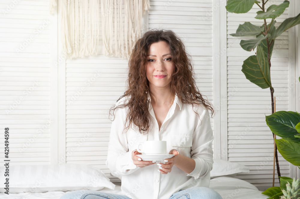 Brunette woman in white clothes is drinking morning coffee in bed Brunette woman in white clothes is drinking morning coffee in bed
