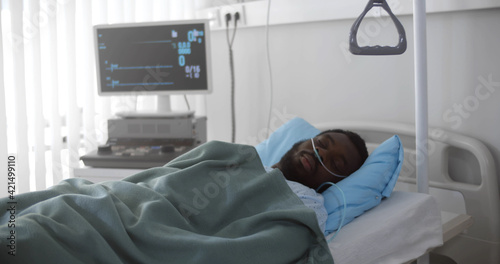 Portrait of afro-american man in coma dying in hospital bed with heart rate falling on ecg monitor
