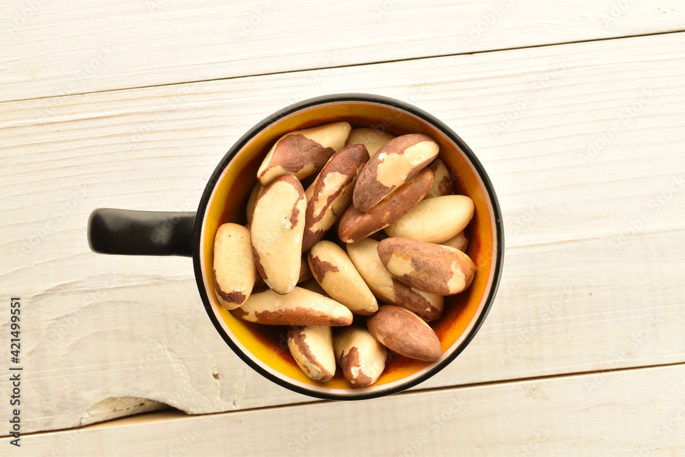 Several delicious organic Brazil nuts with a ceramic cup on a wooden table, close-up, top view. Several delicious organic Brazil nuts with a ceramic cup on a wooden table, close-up, top view.