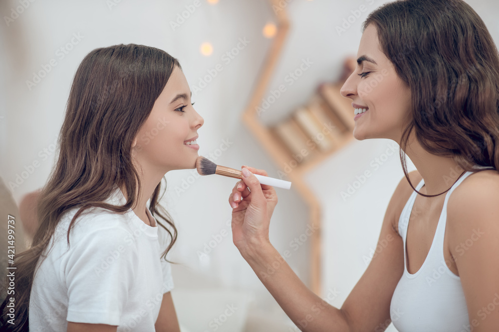 Mom with makeup brush touching chin of teenage daughter Mom with makeup brush touching chin of teenage daughter