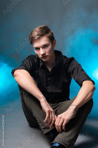 Portrait of a young man on a gray background with blue smoke