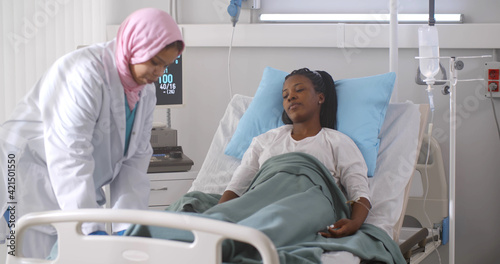 Arabian nurse taking care and checking up african female patient in hospital ward