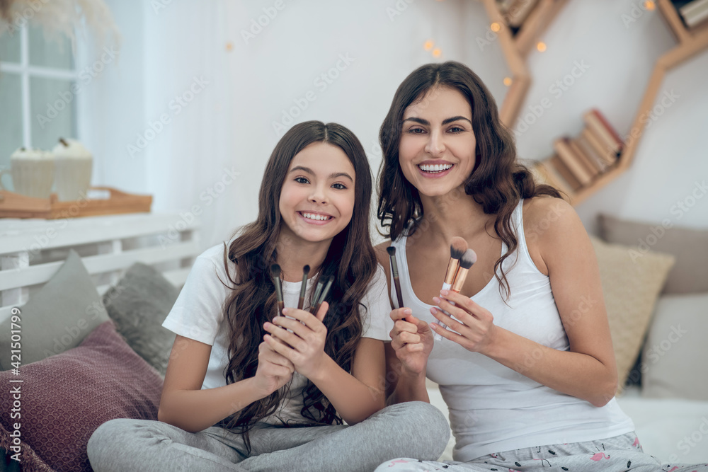 Woman and girl sitting with set of makeup brushes Woman and girl sitting with set of makeup brushes