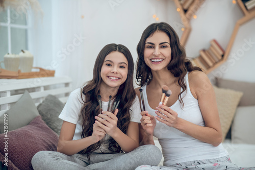 Woman and girl sitting with set of makeup brushes