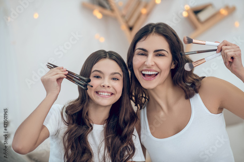 Enthusiastic mom and daughter showing makeup brushes