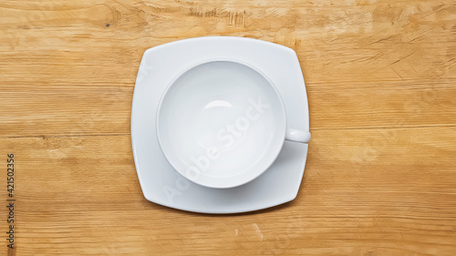 top view of white, empty cup and saucer on wooden surface