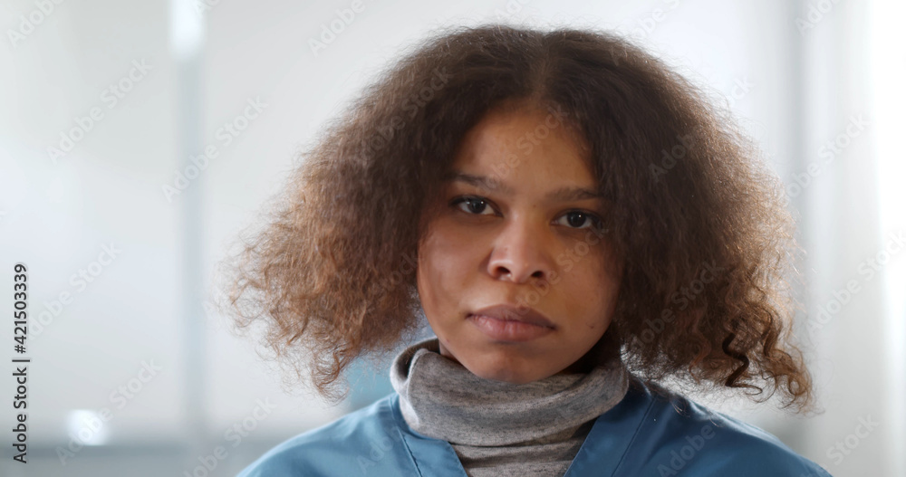 Portrait of young tired afro-american female doctor looking at camera in hospital corridor Portrait of young tired afro-american female doctor looking at camera in hospital corridor
