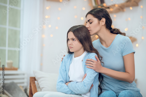 Offended looking away girl and hugging caring mother