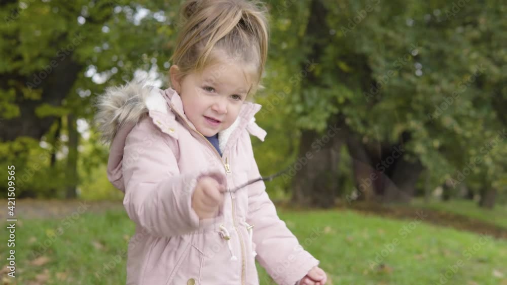 Cute little Caucasian girl plays with a twig and waves it around in a park - closeup Cute little Caucasian girl plays with a twig and waves it around in a park - closeup