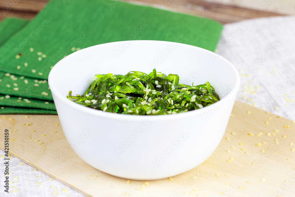 Green Asian seaweed salad in a white bowl on wooden background. Green Asian seaweed salad in a white bowl on wooden background.