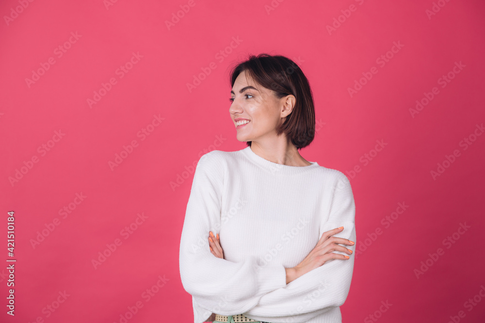 Beautiful woman in casual white sweater on pink red background with crossed hands smile look to left isolated copy space Beautiful woman in casual white sweater on pink red background with crossed hands smile look to left isolated copy space