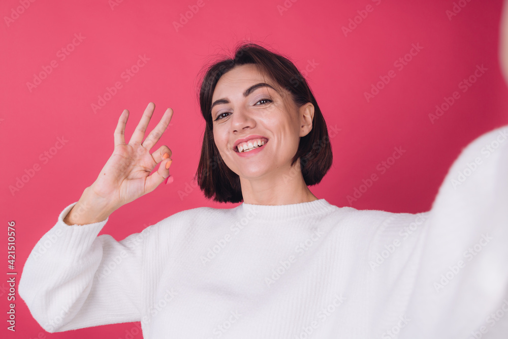 Beautiful woman in casual white sweater on pink red background smile shooting selfie, gesturing ok sign with fingers, having video call isolated copy space Beautiful woman in casual white sweater on pink red background smile shooting selfie, gesturing ok sign with fingers, having video call isolated copy space