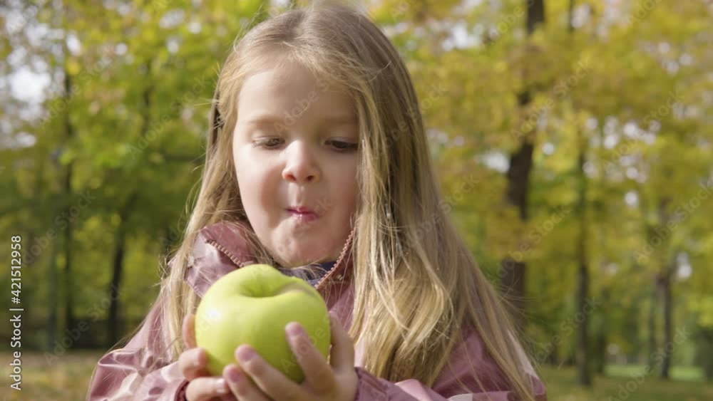 Cute little Caucasian girl eats an apple in a park - closeup Cute little Caucasian girl eats an apple in a park - closeup