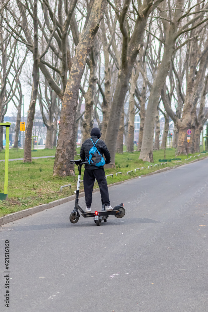 Fototapeta premium Young man on electric scooter with a second scooter for recharge working as juicer in urban city life style of eco friendly transportation and future mobility in hipster gadget zones as trendy motor