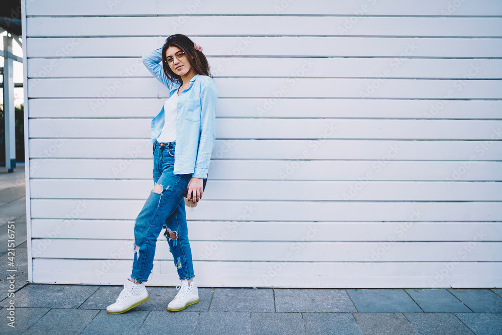 Full length portrait of stylish Caucasian woman 20 years old dressed in casual wear posing outdoors, attractive hipster girl holding takeaway coffee to go in hand looking at camera at urban setting