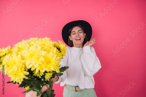 Stylish woman in hat and casual white sweater on pink red background gets large bouquet of yellow flowers, spring mood, isolated space amazed excited surprised © Анастасия Каргаполов