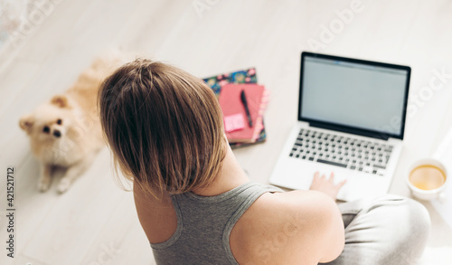 Work from home and pets. Pomeranian spitz and a young woman working with a laptop on a wooden floor.