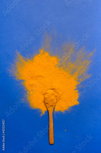 Top view of powdered turmeric, wooden spoon on the bright blue surface