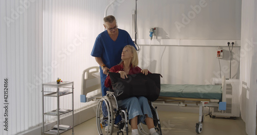 Male orderly pushing senior female patient being discharged from hospital in wheelchair