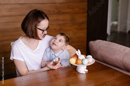 Mom and disabled son are painting Easter eggs in a lifestyle photo. child with cerebral palsy celebrates Easter at home. Happy family together. Inclusion. Kindness, mercy, care and happiness. autism 