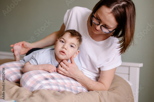 Mother gives a massage to child with cerebral palsy. Rehabilitation therapy at home. Developing leisure activities. Disabled child epilepsy autism. Moments of life. Lifestyle. Hope support love family