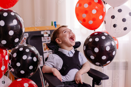 Happy Boy with cerebral palsy celebrates his birthday. Disabled person in a wheelchair in air balloons happy. Inclusion. Lifestyle photo is real. Moments of life at home. Child happy toddler laughs. 