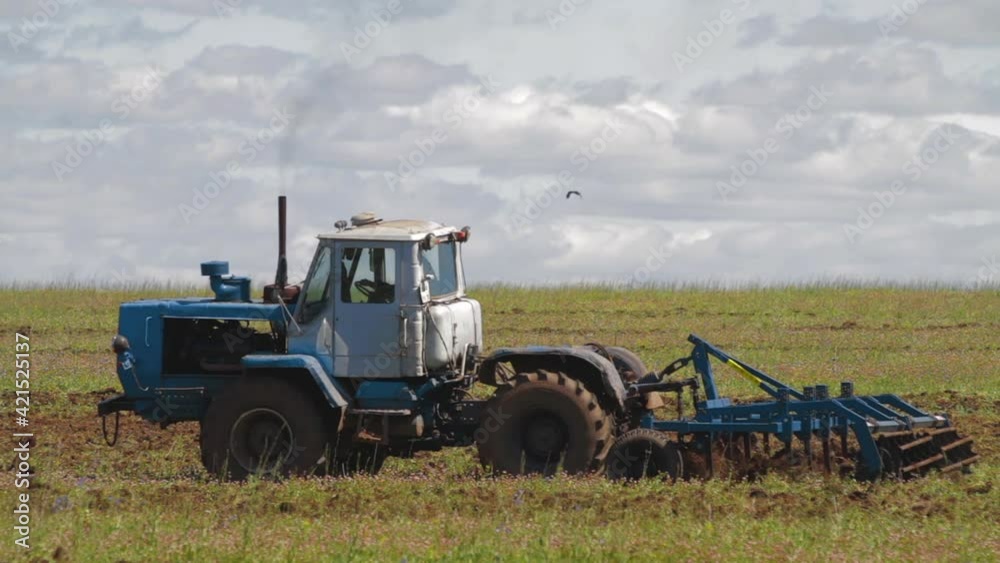 Tractor cuts furrows in farm field for sowing farm tractor with rotary harrow plow preparing land for sowing. Tractor with harrows prepares the agricultural land for planting crop Tractor cuts furrows in farm field for sowing farm tractor with rotary harrow plow preparing land for sowing. Tractor with harrows prepares the agricultural land for planting crop